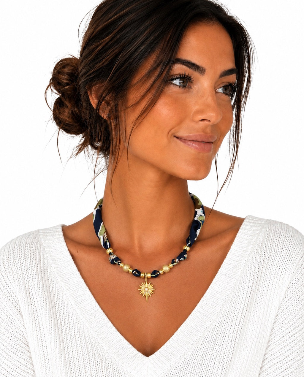 A woman wearing a beaded necklace with a gold sunburst pendant and a patterned fabric section, shown against a plain white background.