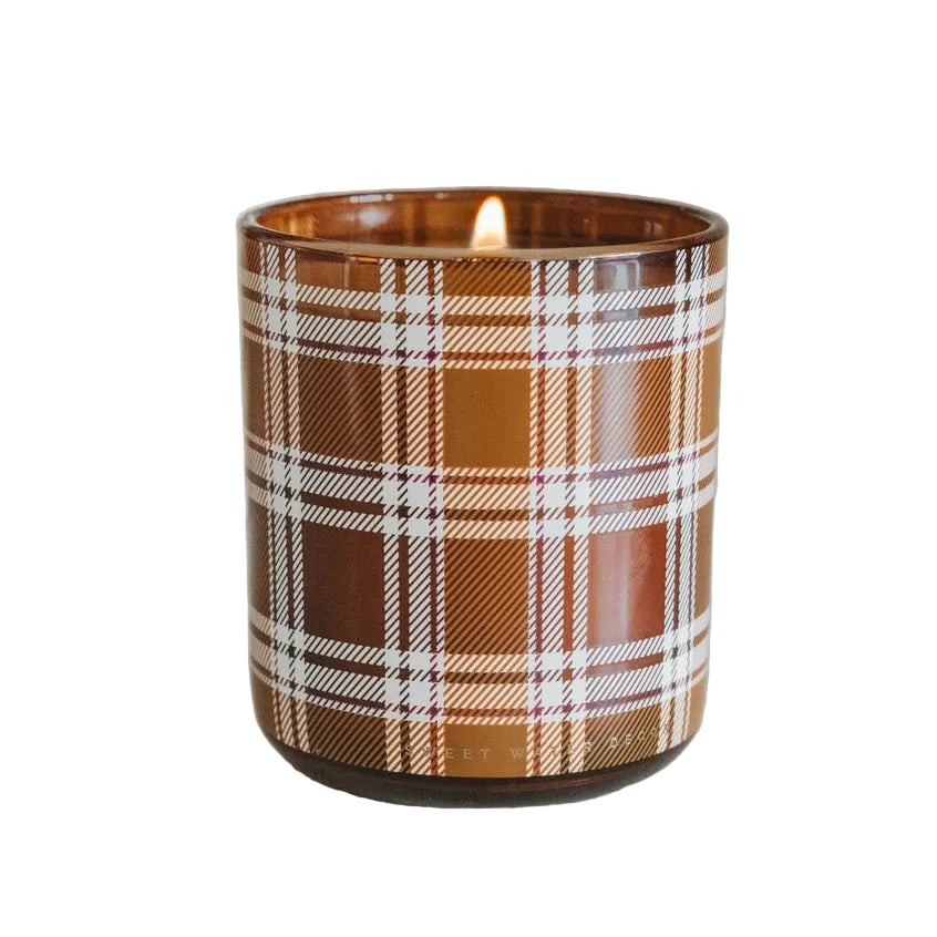 A lit candle in a brown glass jar with a white and brown plaid pattern, set against a white background.