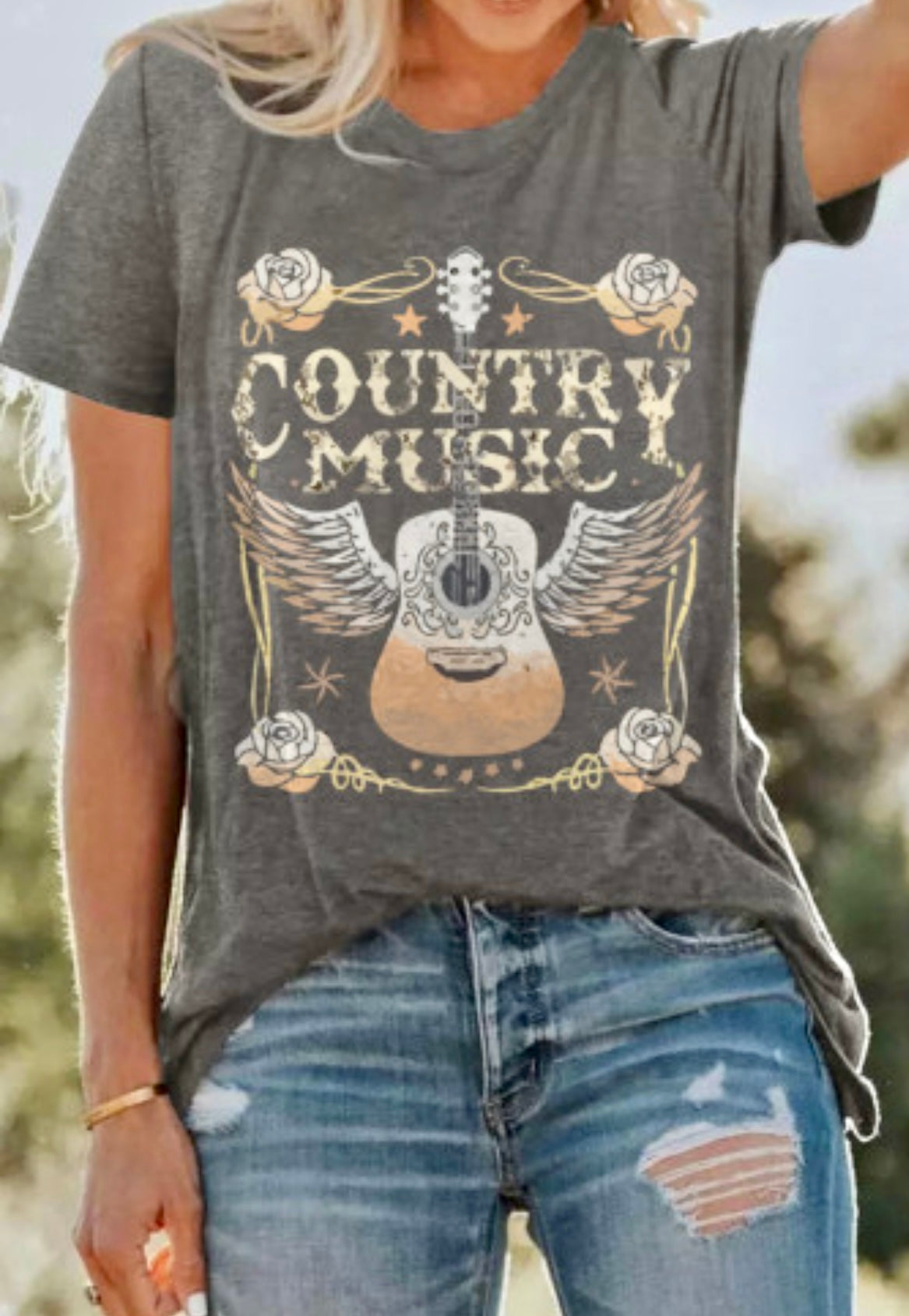 Person wearing a gray t-shirt with 'Country Music' and guitar design outdoors.