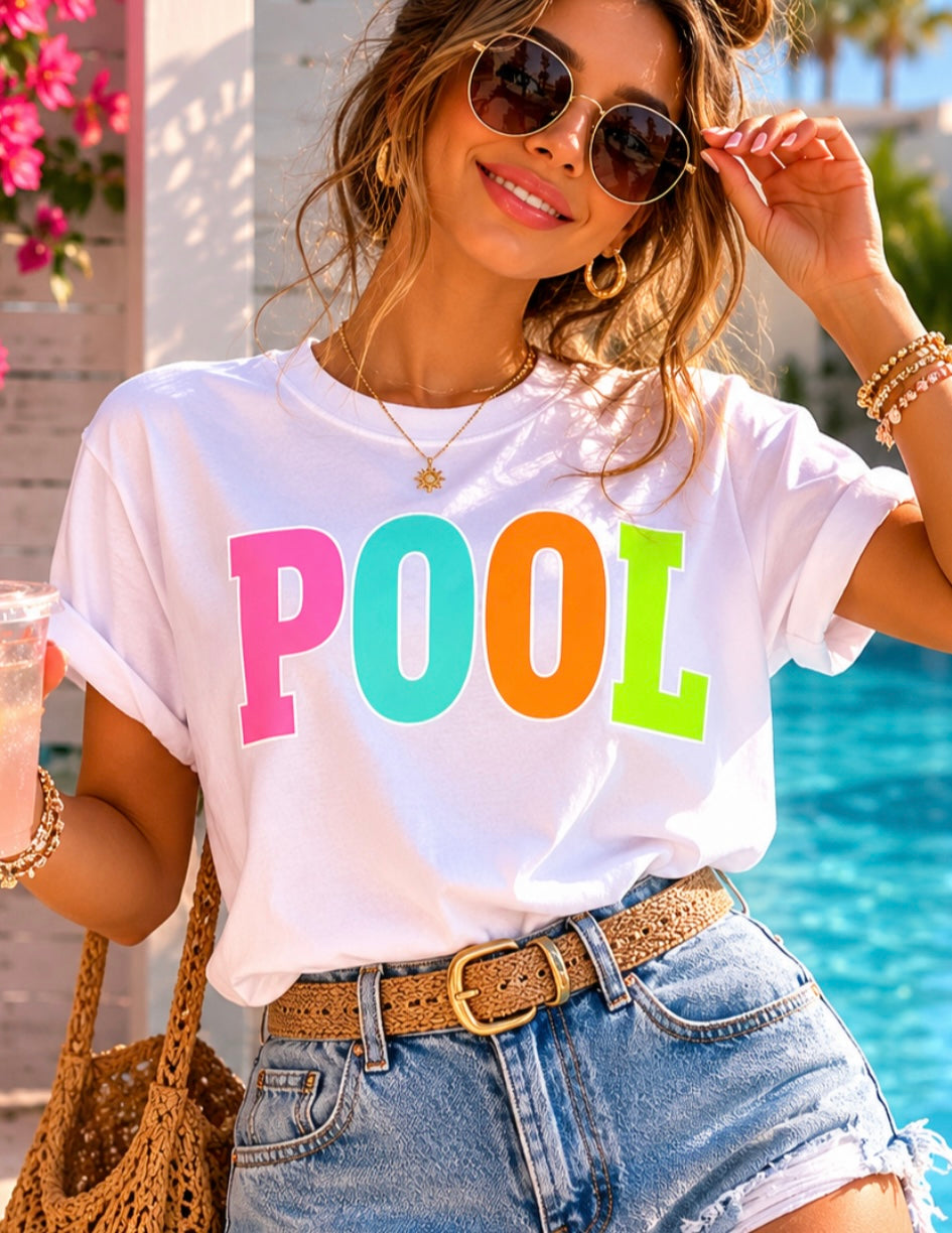 Woman wearing a white t-shirt with colorful 'POOL' text by a poolside.