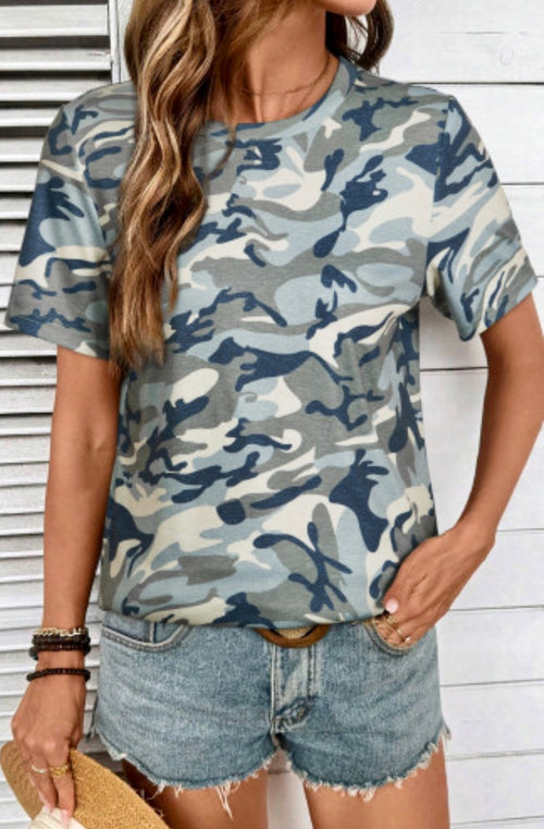 Woman wearing a camouflage t-shirt and denim shorts against a white wooden background