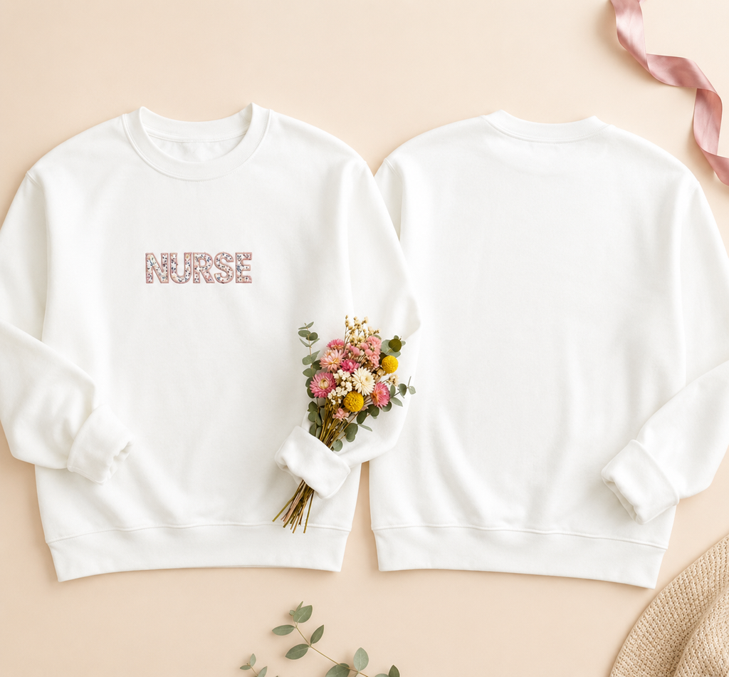 White sweatshirt with 'Nurse' and 'Nurse Mom' text, accompanied by a bouquet of flowers on a beige background.