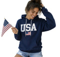 Woman wearing a navy blue 'USA' hoodie holding a flag with a white background.