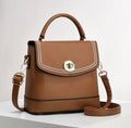 A brown pebbled leather handbag with a top handle, a detachable shoulder strap, and a silver-tone metal logo clasp on the front flap, displayed on a white surface against a light gray background.