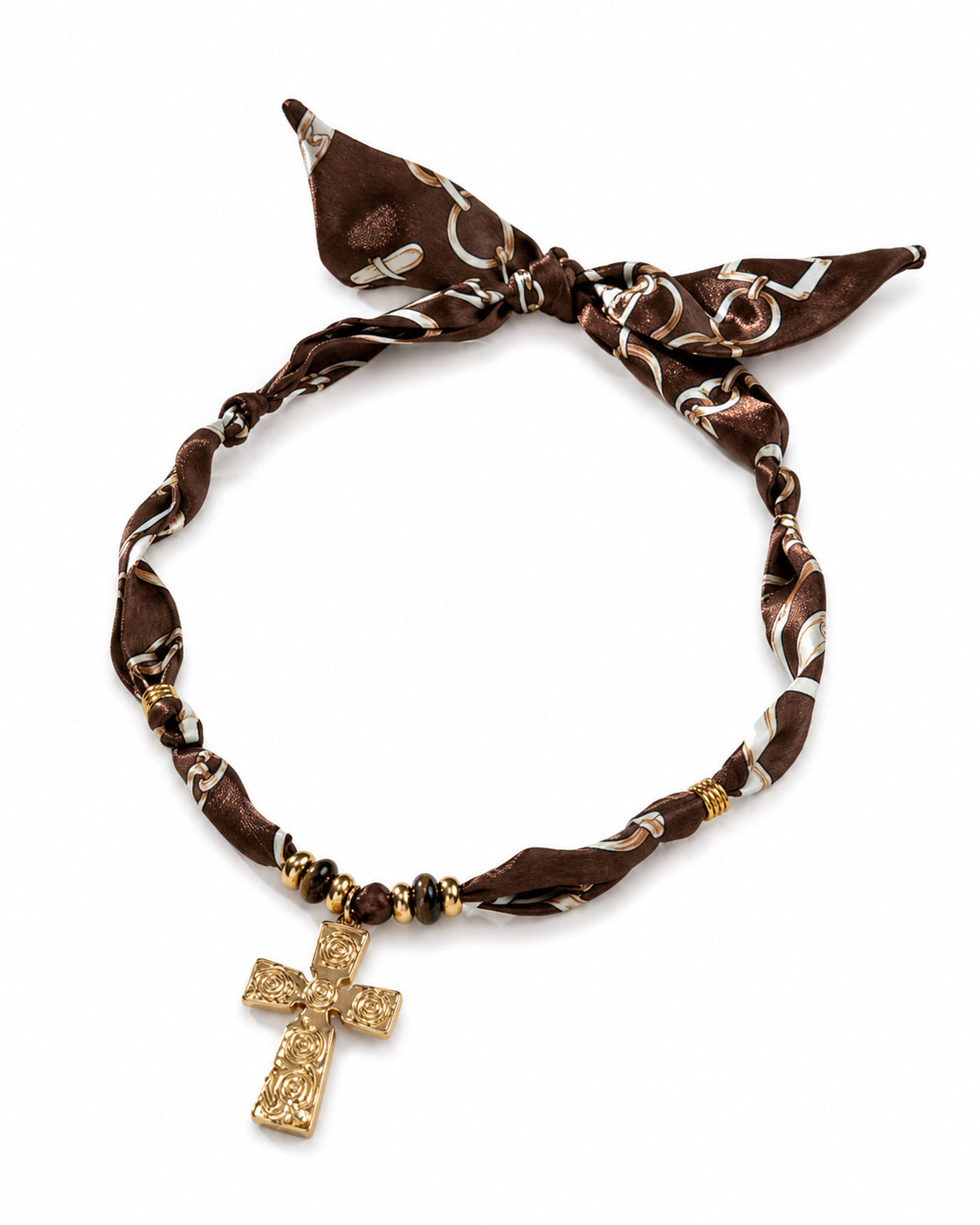 A brown silk scarf necklace with a white and brown pattern, tied in a knot at the top and featuring a dangling gold cross pendant.