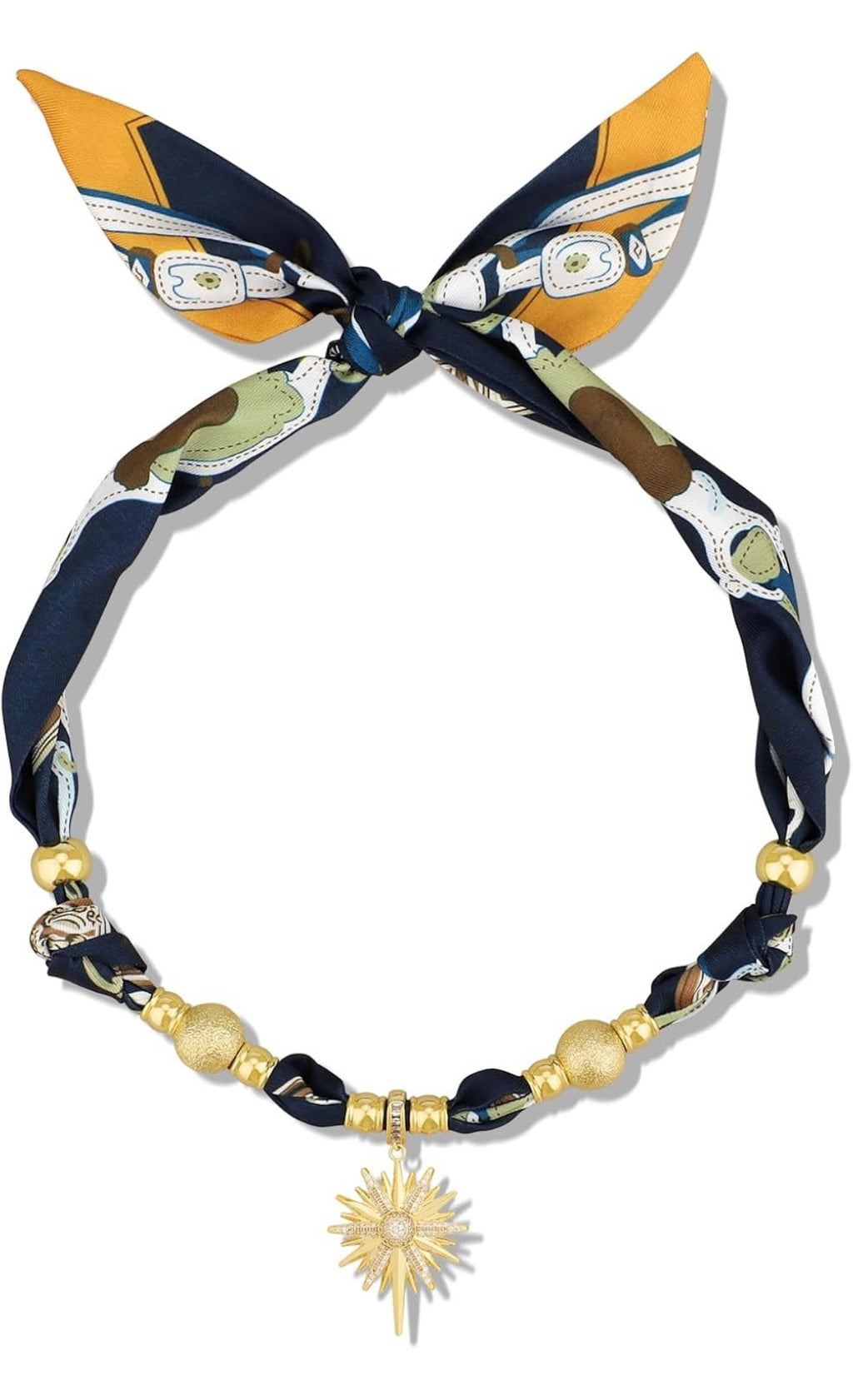 A fashion scarf styled as a necklace, featuring a navy blue and mustard yellow patterned silk scarf tied in a bow at the top, adorned with gold-toned beads and a gold sunburst charm, set against a plain white background.