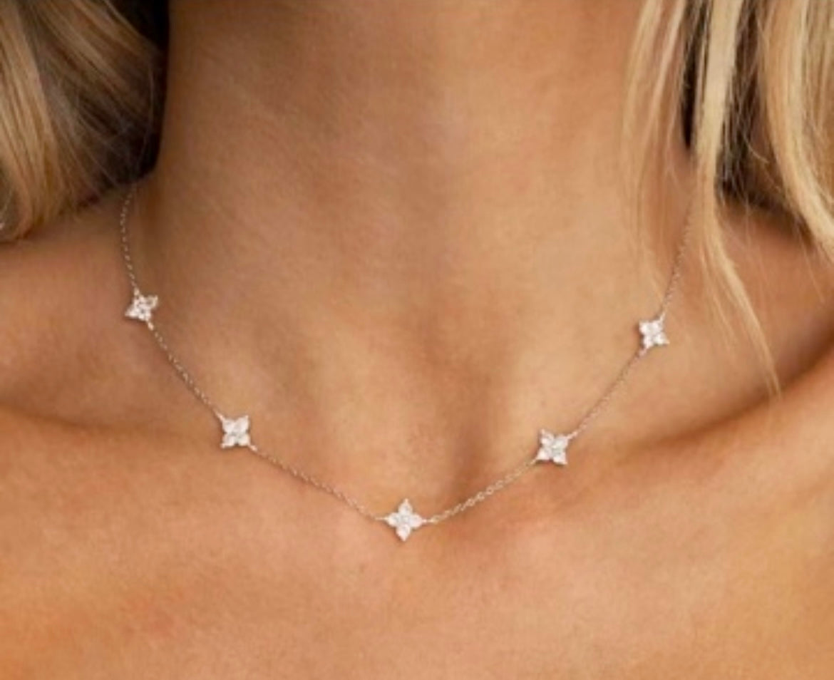A delicate silver necklace with five small star-shaped charms, shown worn on a model's neck.