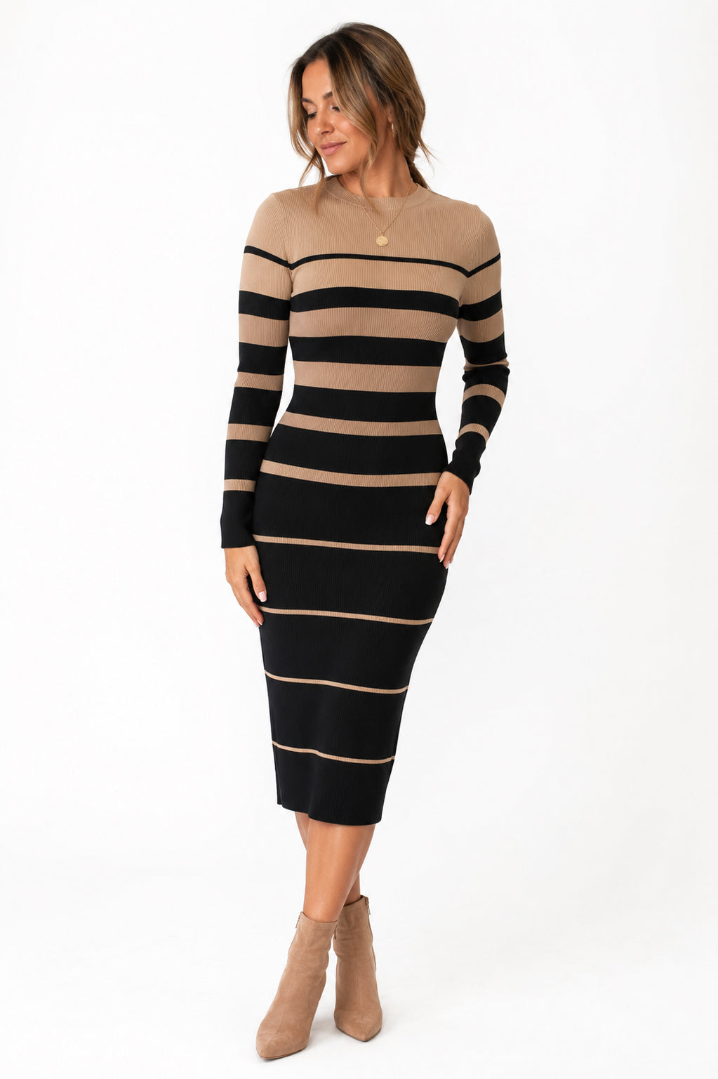 A woman modeling a fitted long-sleeve knit midi dress with horizontal black and tan stripes, paired with tan ankle boots, against a plain white studio background.