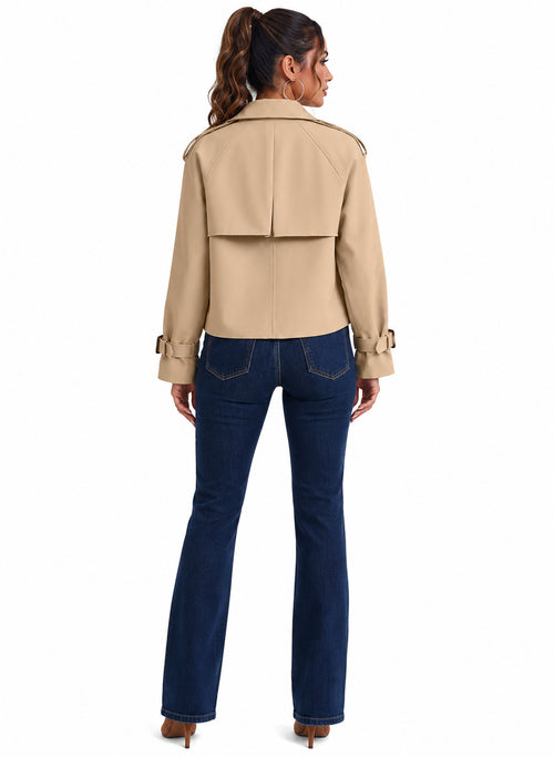 A woman shown from the back wearing a cropped beige trench-style jacket and dark blue flare jeans against a plain white studio background.