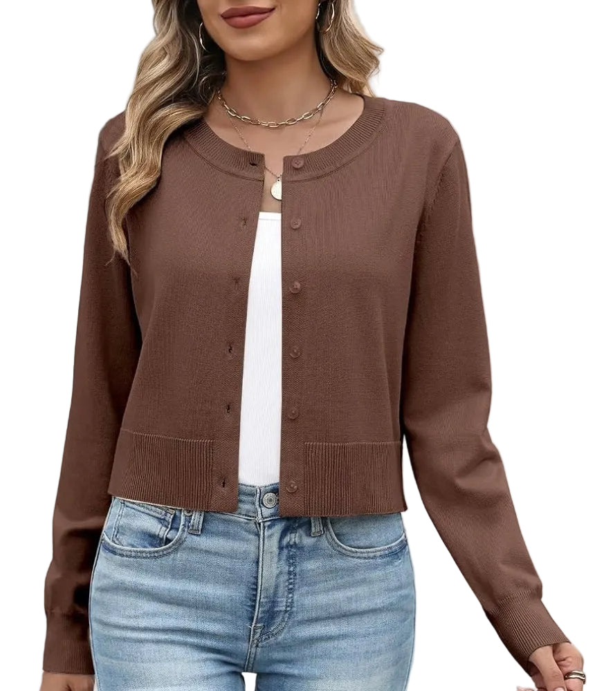 A woman wearing a brown long-sleeve cropped cardigan with a round neckline and front buttons, layered over a white top and paired with light blue jeans with a white  background.