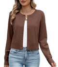 A woman wearing a brown long-sleeve cropped cardigan with a round neckline and front buttons, layered over a white top and paired with light blue jeans with a white  background.