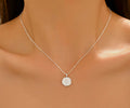 A delicate silver chain necklace with a small, flat circular pendant featuring an engraved monogram, shown worn on a model's neck.