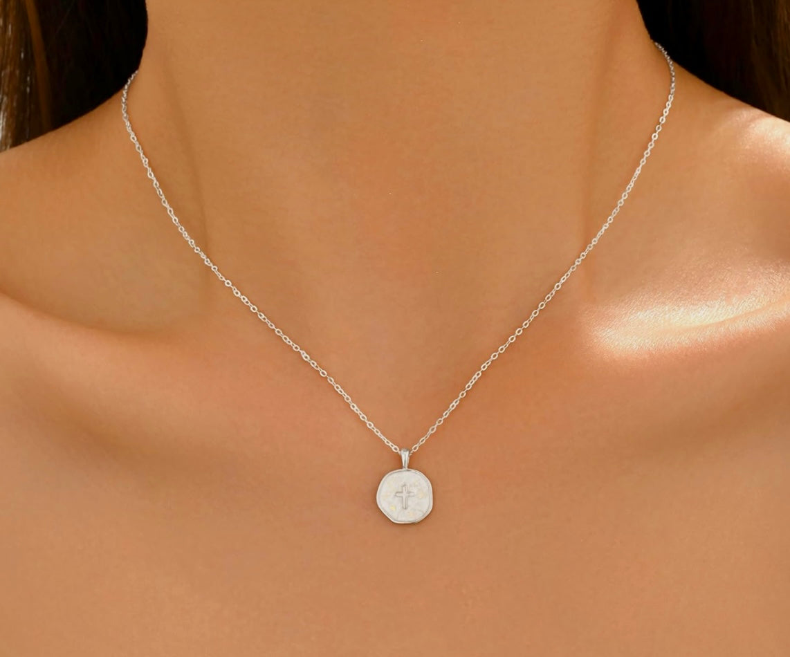 A delicate silver chain necklace with a small, flat circular pendant featuring an engraved monogram, shown worn on a model's neck.