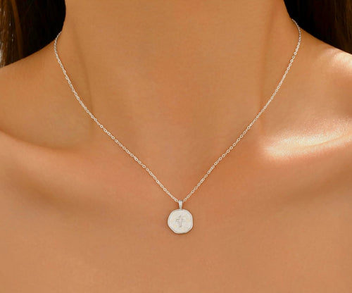 A delicate silver chain necklace with a small, flat circular pendant featuring an engraved monogram, shown worn on a model's neck.