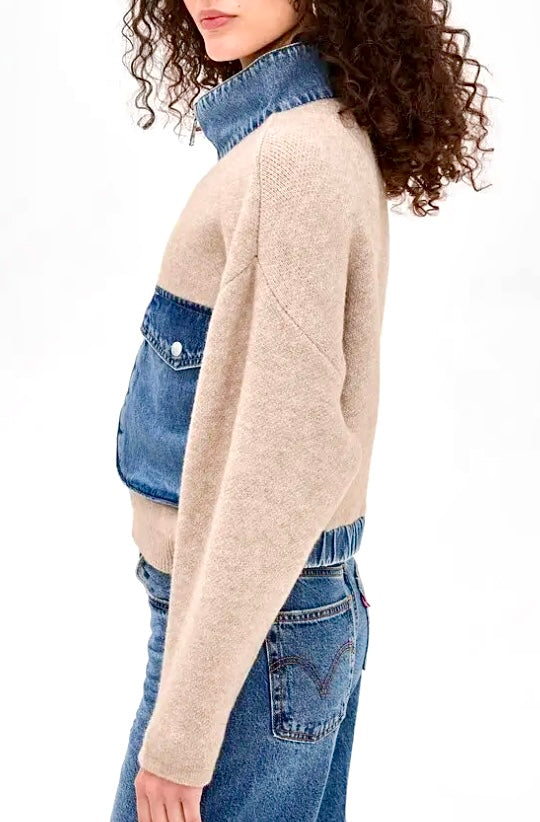 A woman shown from the side wearing a knit mock-neck sweater with a beige body and blue denim paneling on the chest and collar, paired with blue jeans against a plain white background.