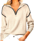 A woman wearing a light beige heathered quarter-zip pullover sweatshirt with black contrast piping along the shoulders and collar, paired with white pants.