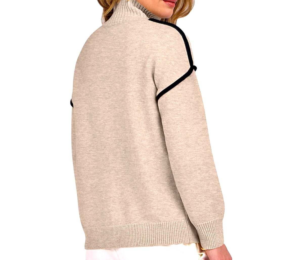 A woman wearing a beige knit turtleneck sweater with black contrast trim along the shoulder and sleeve, shown from a side-back angle against a plain white background.