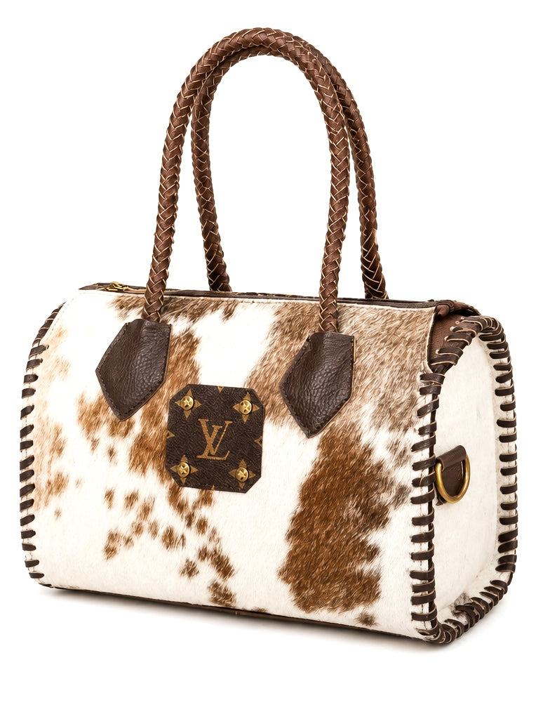 Upcycled Louis Vuitton cowhide handbag with brown braided handles, a brown leather LV monogram patch on the front, and whipstitched edges on a white background.