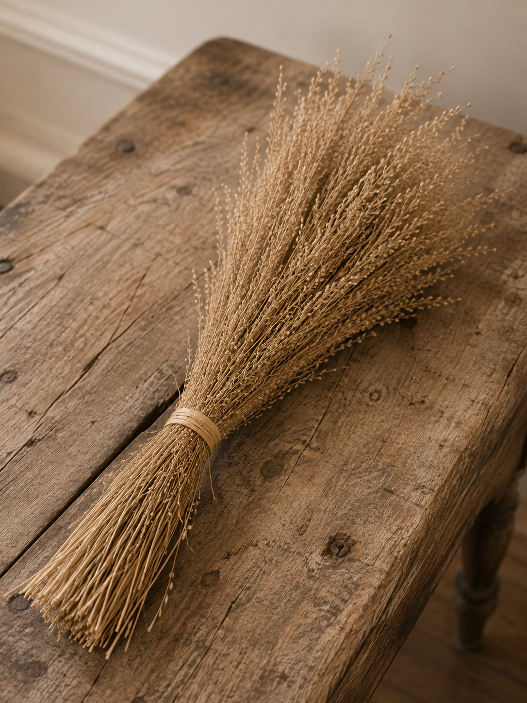 A small dried wheat or grass bundle tied with a simple band, resting diagonally on a rustic wooden table.