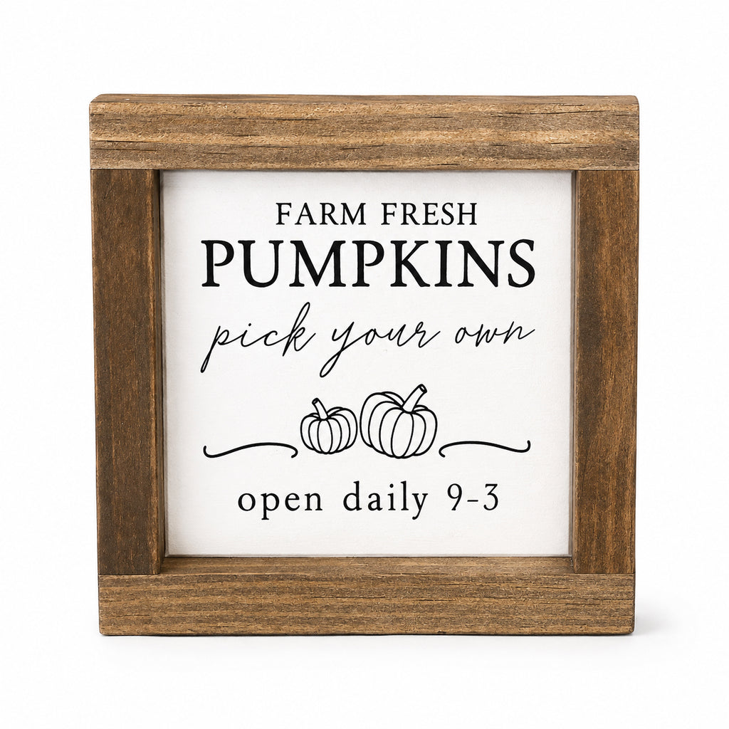 Square wooden sign with a white insert featuring the text 'FARM FRESH PUMPKINS pick your own open daily 9-3' and simple pumpkin illustrations, shown on a light gray background.