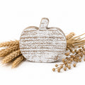 A distressed white and brown faux-wood pumpkin-shaped decorative sign styled with dried wheat stalks and baby's breath on a white background.