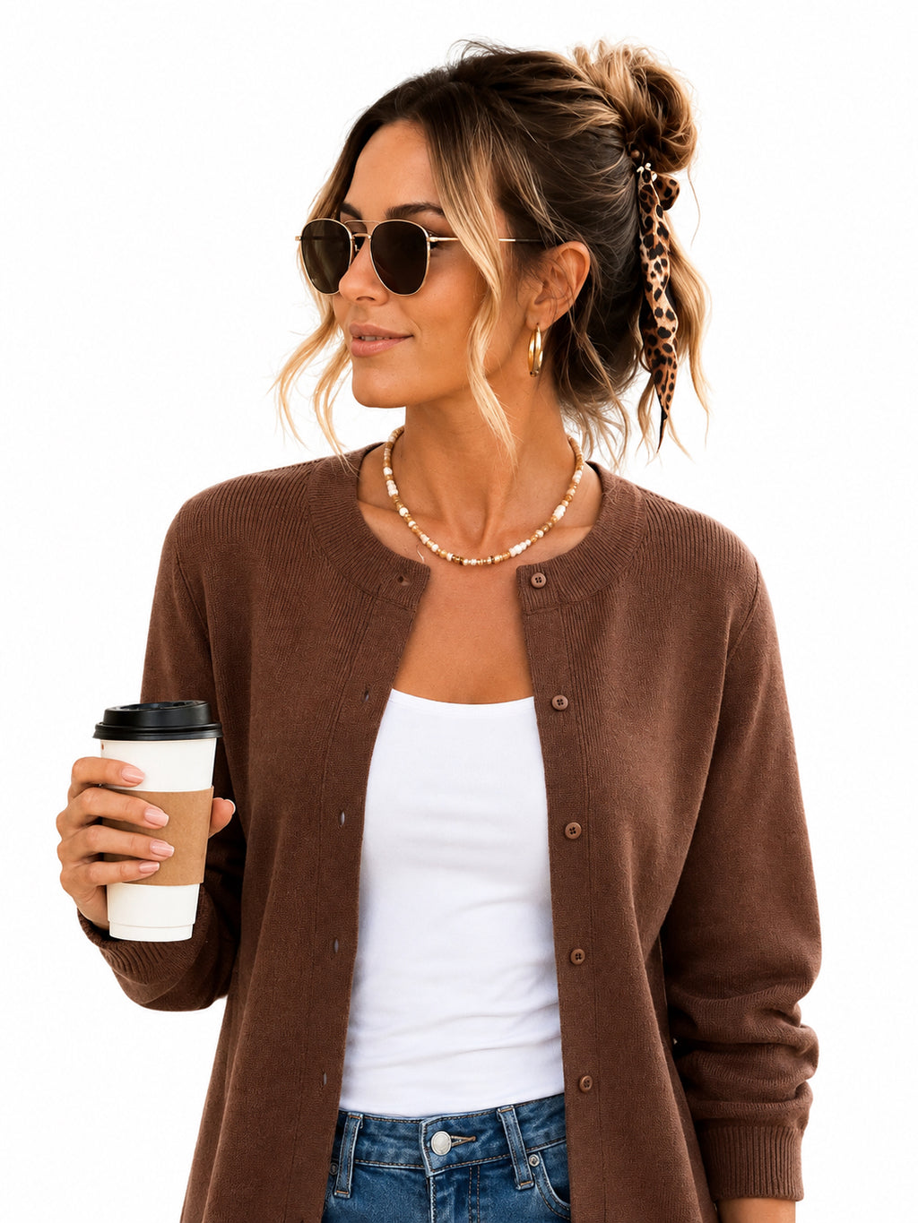 A woman wearing a brown button-up cardigan over a white tank top and blue jeans, holding a coffee cup against a plain white background.