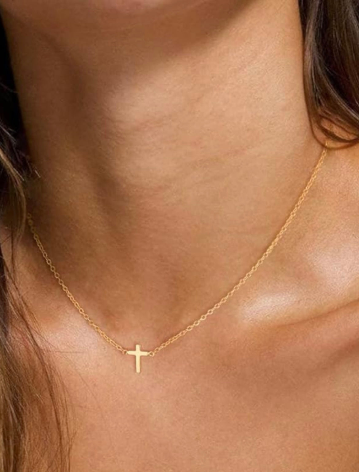 A close-up of a delicate gold chain necklace with a small cross pendant worn on a person's neck.