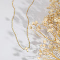 A delicate gold cross pendant necklace on a fine gold chain, styled on a white surface next to dried baby's breath flowers.