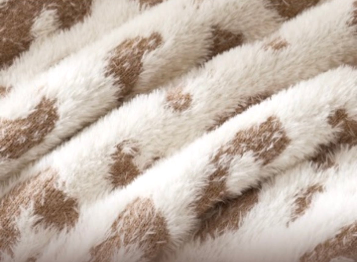 Close-up of a plush faux-fur textile with a white base and irregular tan-brown spots, showing the soft texture and pattern in detail.