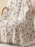 A plush throw blanket with a brown leopard print pattern draped over a wooden chair in a cozy indoor setting.