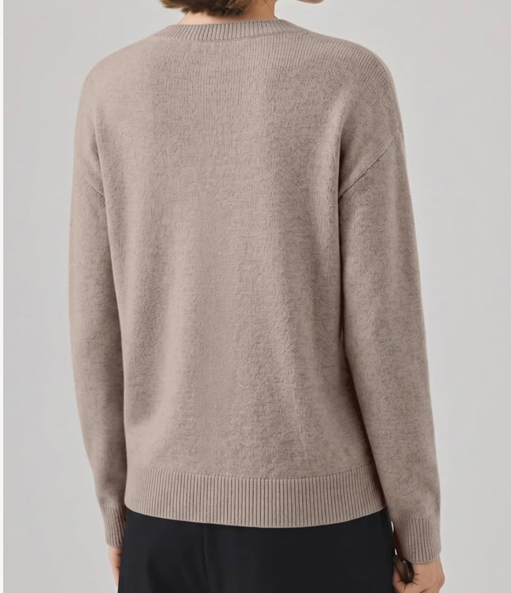 A person shown from the back wearing a light taupe knit sweater with ribbed collar, cuffs, and hem, paired with dark pants against a plain light gray studio background.