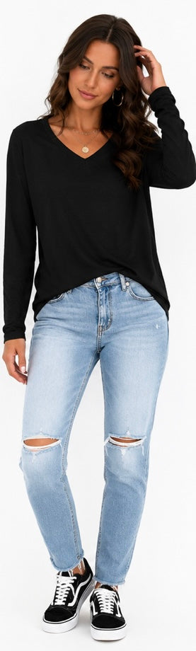 A woman modeling a black long-sleeve V-neck top, light-wash distressed blue jeans, and black sneakers against a plain white background.