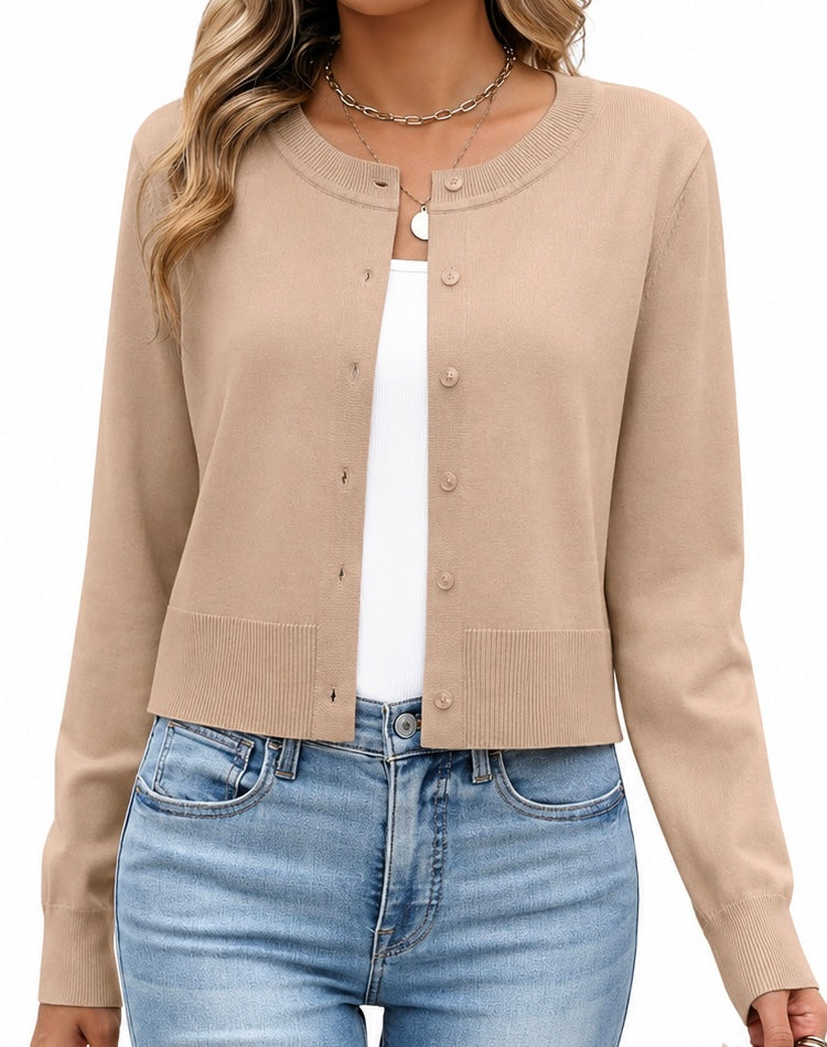 A woman wearing a beige cardigan sweater with a crew neck, button front, and ribbed cuffs and hem, layered over a white top and paired with light blue jeans.