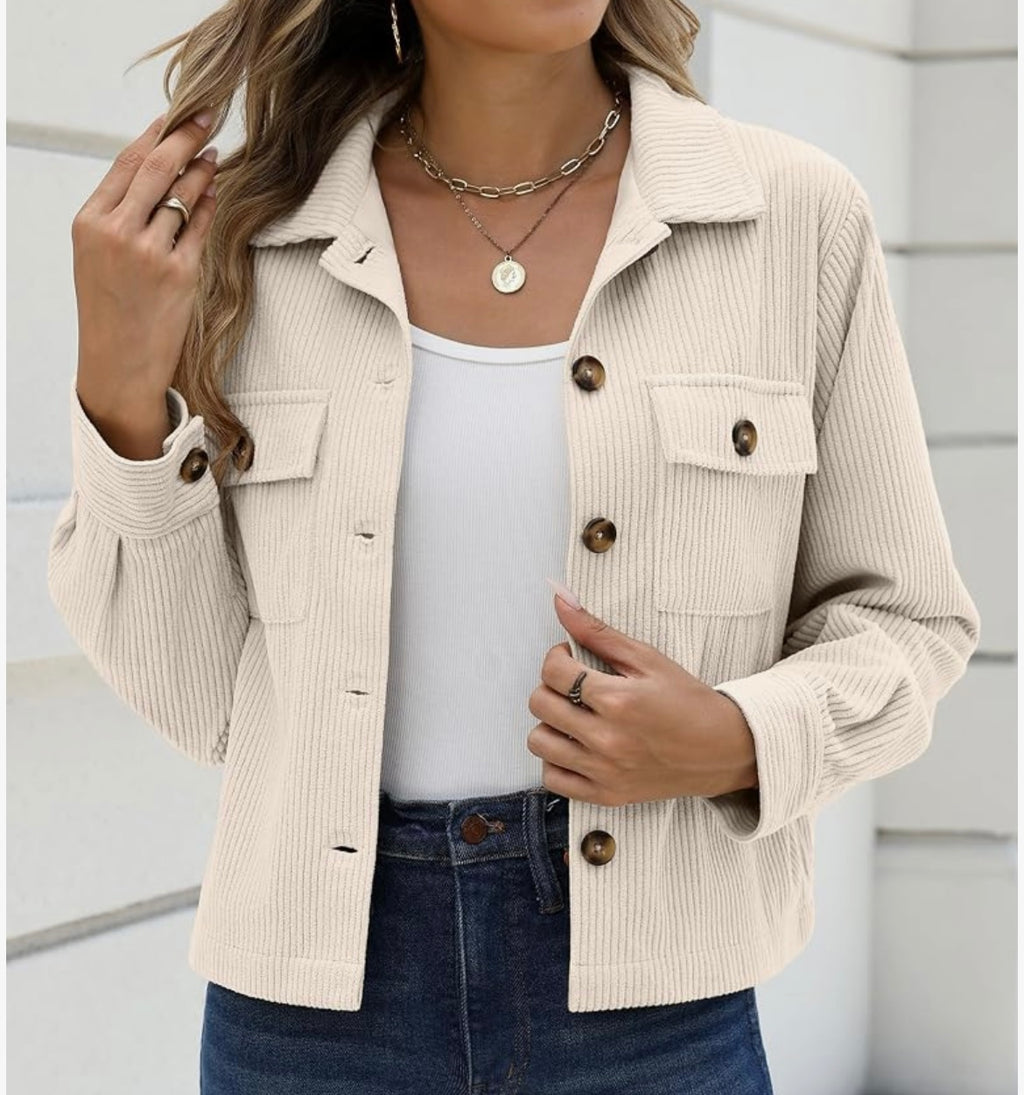 A woman wearing a ribbed knit button-front jacket in a light cream color, styled over a white tank top and dark blue jeans.