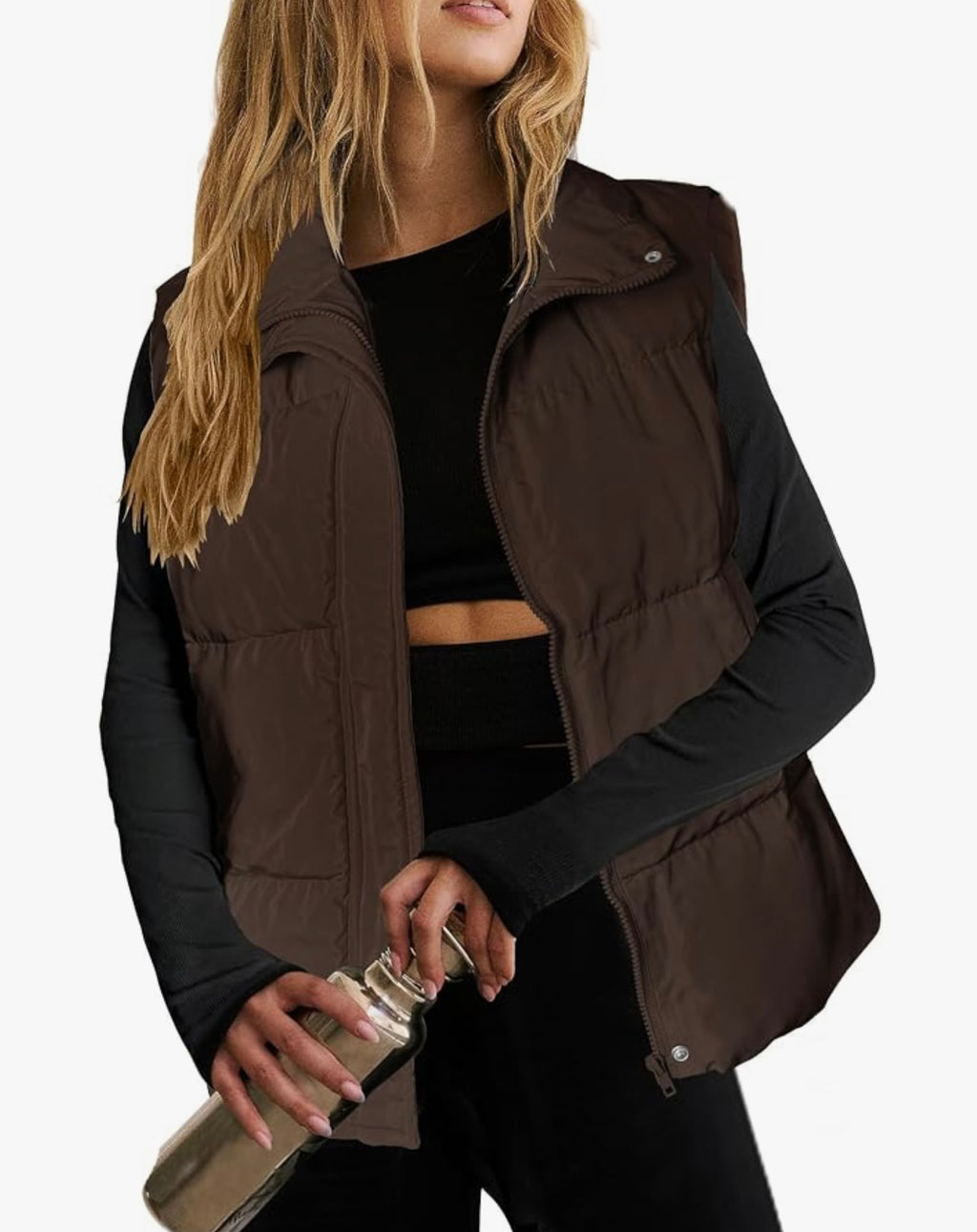 A woman wearing a dark brown puffer vest over a black long-sleeve crop top and black leggings, holding a metallic water bottle against a plain white background.