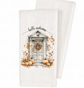 A white kitchen tea towel featuring a watercolor-style autumn door illustration with pumpkins, falling leaves, a wreath, and the words 'hello autumn' in black script. A second folded towel is partially visible behind it on a clean white background.