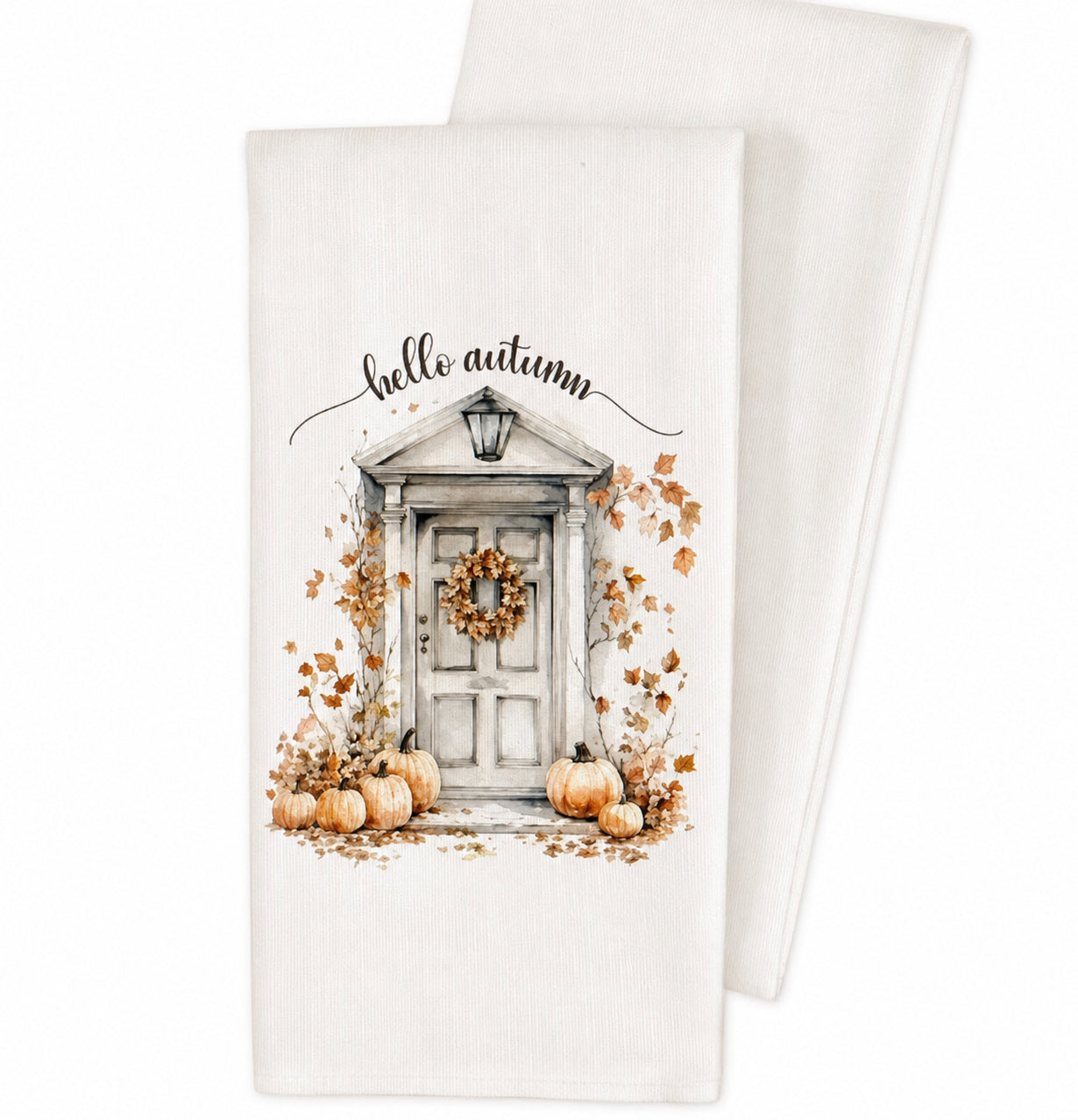 A white kitchen tea towel featuring a watercolor-style autumn door illustration with pumpkins, falling leaves, a wreath, and the words 'hello autumn' in black script. A second folded towel is partially visible behind it on a clean white background.