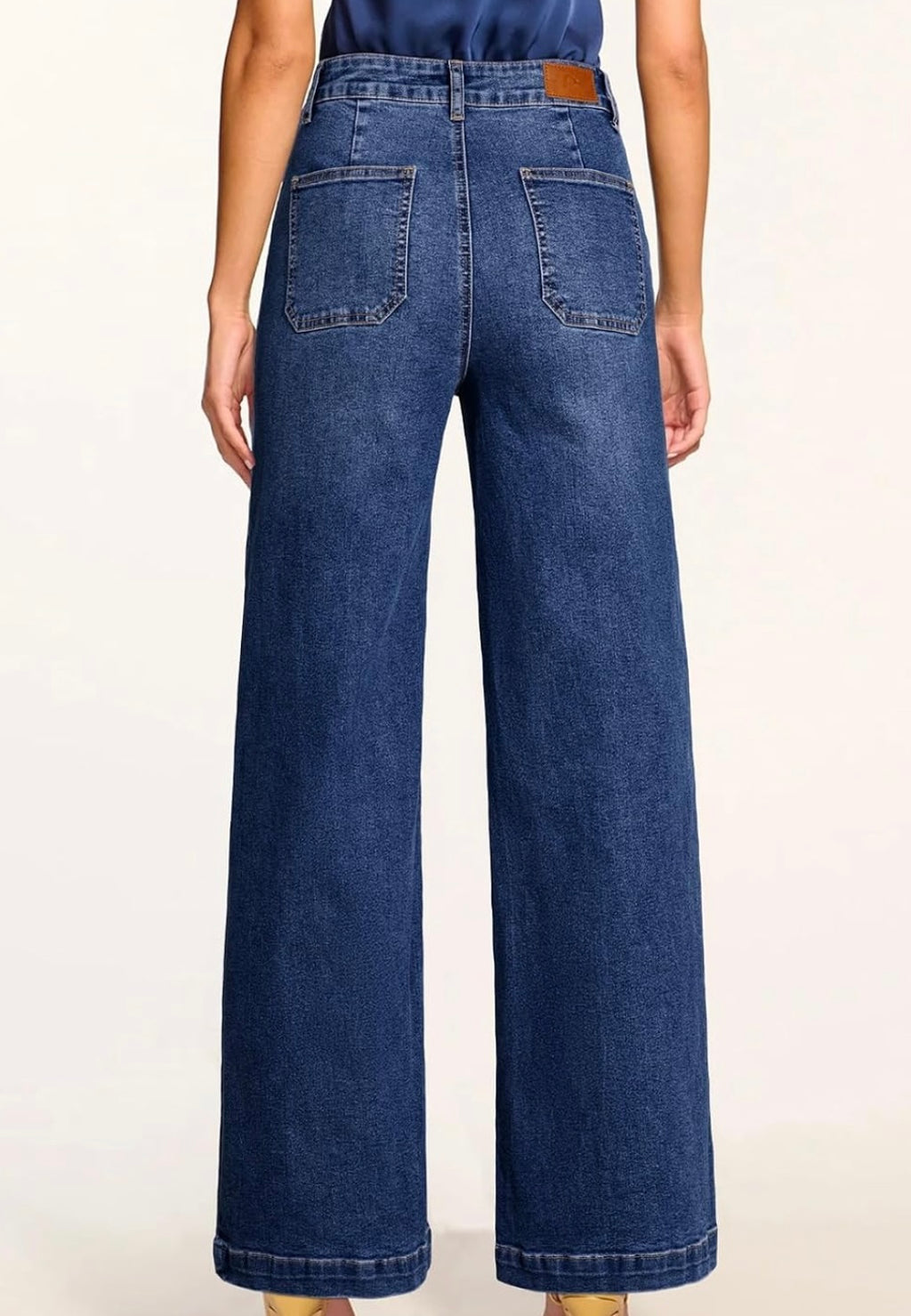 A person shown from the back wearing dark blue wide-leg denim jeans with a brown leather patch at the back waistband, against a plain light background.
