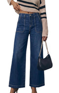 A model wearing high-waisted, wide-leg blue denim jeans with front patch pockets, styled with a beige and navy striped knit sweater and a black shoulder bag with a gold chain strap.