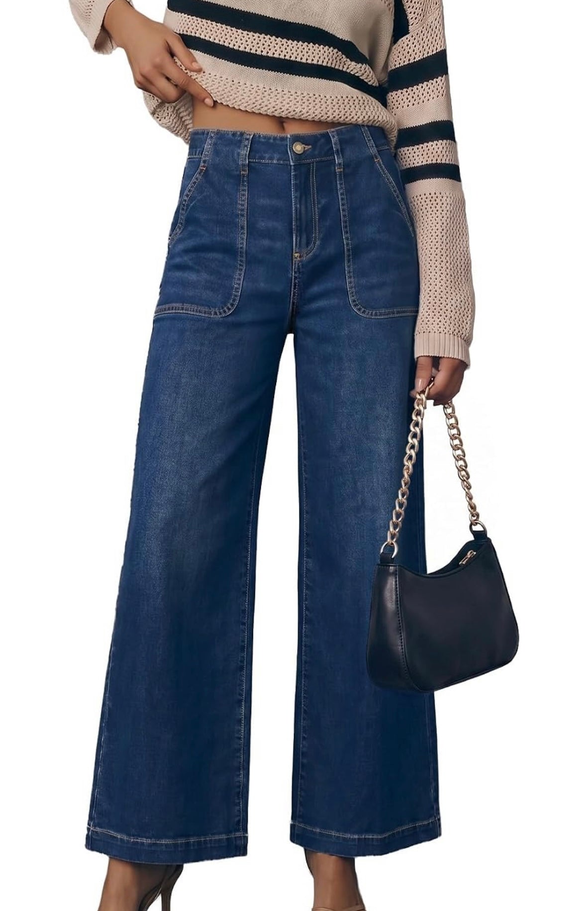 A model wearing high-waisted, wide-leg blue denim jeans with front patch pockets, styled with a beige and navy striped knit sweater and a black shoulder bag with a gold chain strap.