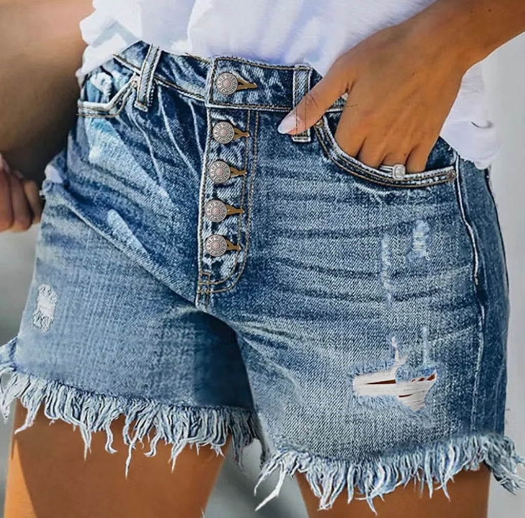 Close-up of a person wearing light blue distressed denim shorts with a button fly, frayed hem, and ripped details, paired with a white top.