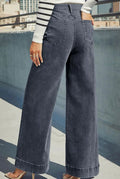 A person wearing dark gray wide-leg denim jeans, shown from the back in an outdoor urban setting with a concrete wall and buildings in the background.